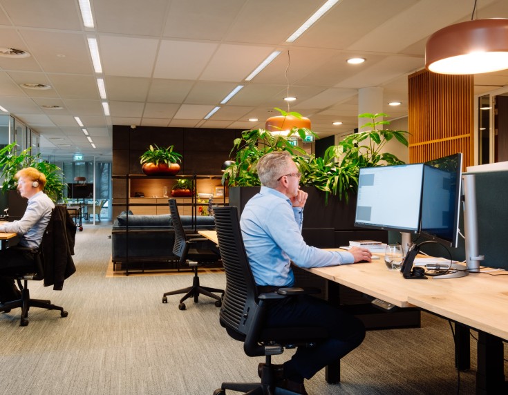 Medewerkers werken aan bureaus in moderne kantoorruimte met planten en warme verlichting.