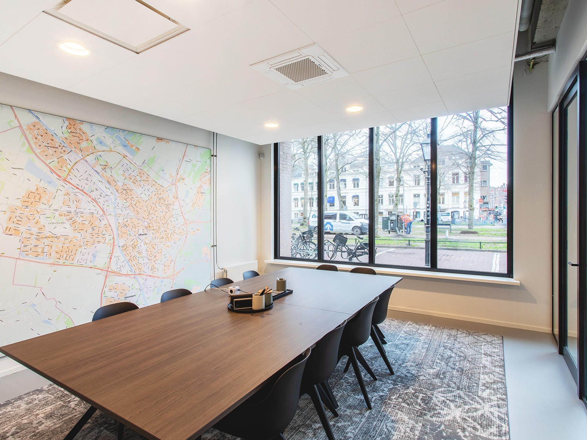 Moderne vergaderruimte met grote tafel, wandkaart en grote ramen met uitzicht op buiten, voorzien van veel daglicht.