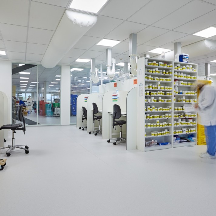 Witte cleanroom met glazen wanden, laboratoriumtafels en heldere verlichting.