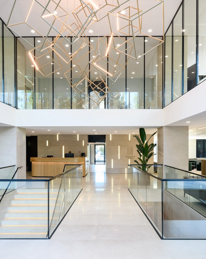 Moderne lobby met glazen balustrades, open vide en opvallende geometrische hanglampen, met een strakke balie op de achtergrond.