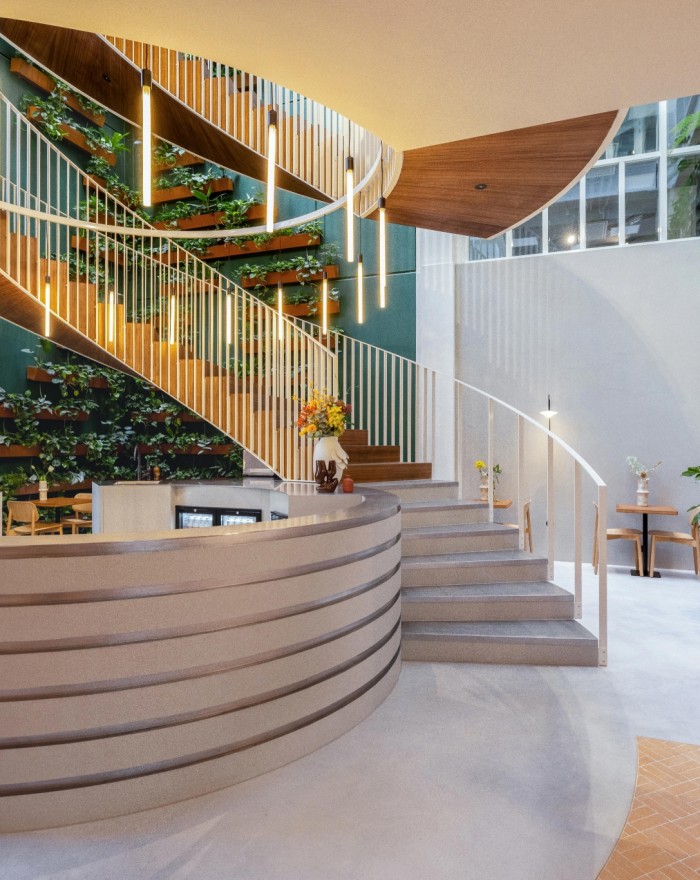 Moderne ontvangsthal met ronde balie, houten trap met groene planten en stijlvolle verlichting voor een warme, uitnodigende uitstraling.