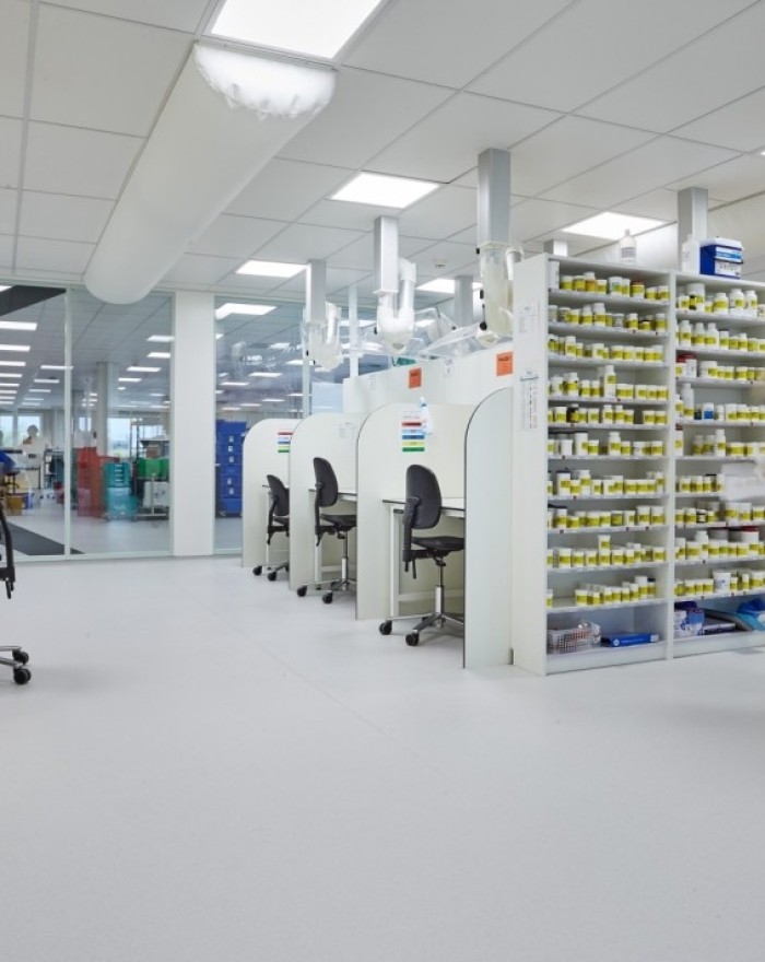 Clean industrial workspace with automated machinery, organized storage racks filled with components, and a worker in protective clothing operating equipment.