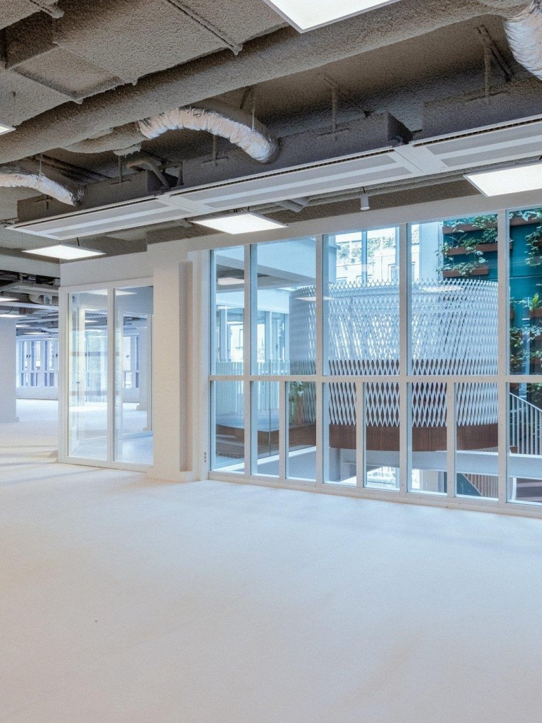 Lege kantoorruimte met grote glazen schuifdeuren, zichtbare plafondinstallaties en uitzicht op een buitenruimte met groen.