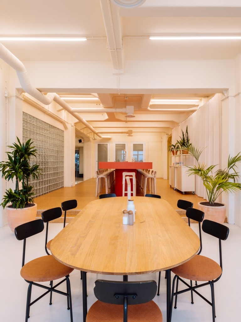 Moderne kantoorruimte met een lange ovale houten tafel, zwarte stoelen, planten, witte gordijnen en een bar in de achtergrond.