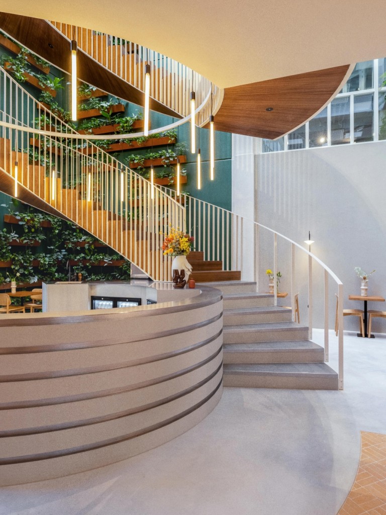 Moderne kantoorentree met een ronde receptiebalie, houten trap met geïntegreerde planten, groene wand en hoge ramen met veel natuurlijk licht.