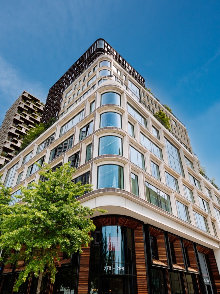 “Modern kantoorgebouw met afgeronde hoek en grote ramen, omringd door bomen tegen een heldere blauwe lucht.