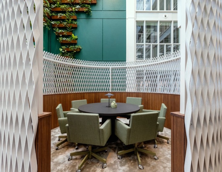 Duurzame vergaderruimte met groene beklede stoelen, houtaccenten en een witte 3D-roomdivider in een groene binnentuinomgeving.