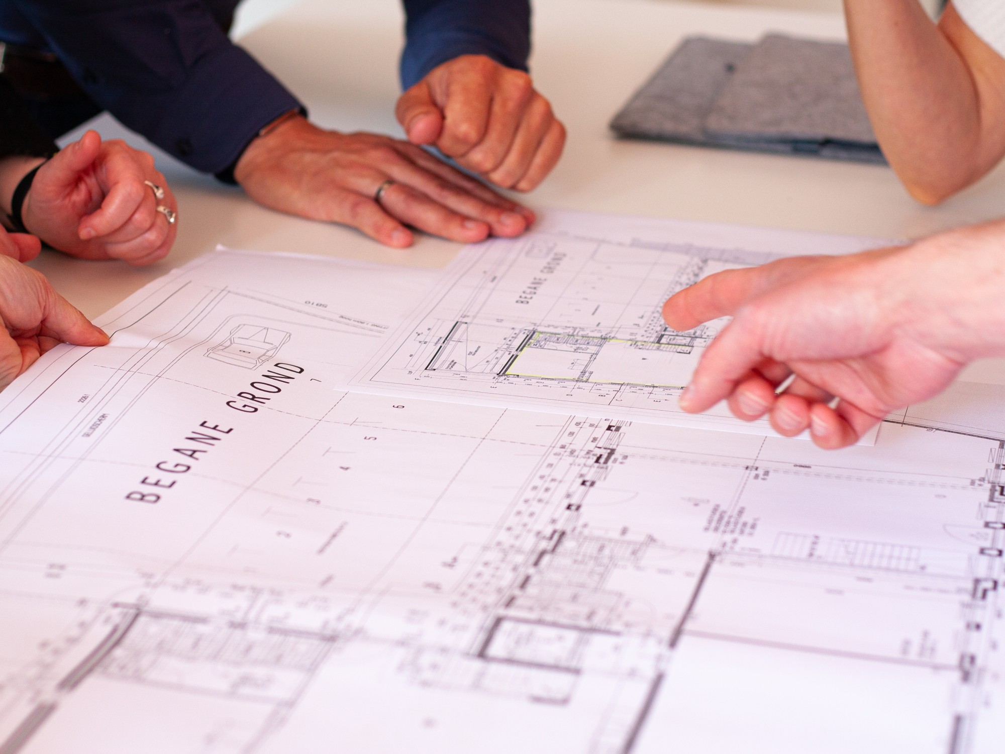 Overlegmoment boven bouwtekeningen waarbij meerdere handen wijzen naar details op de plattegrond.