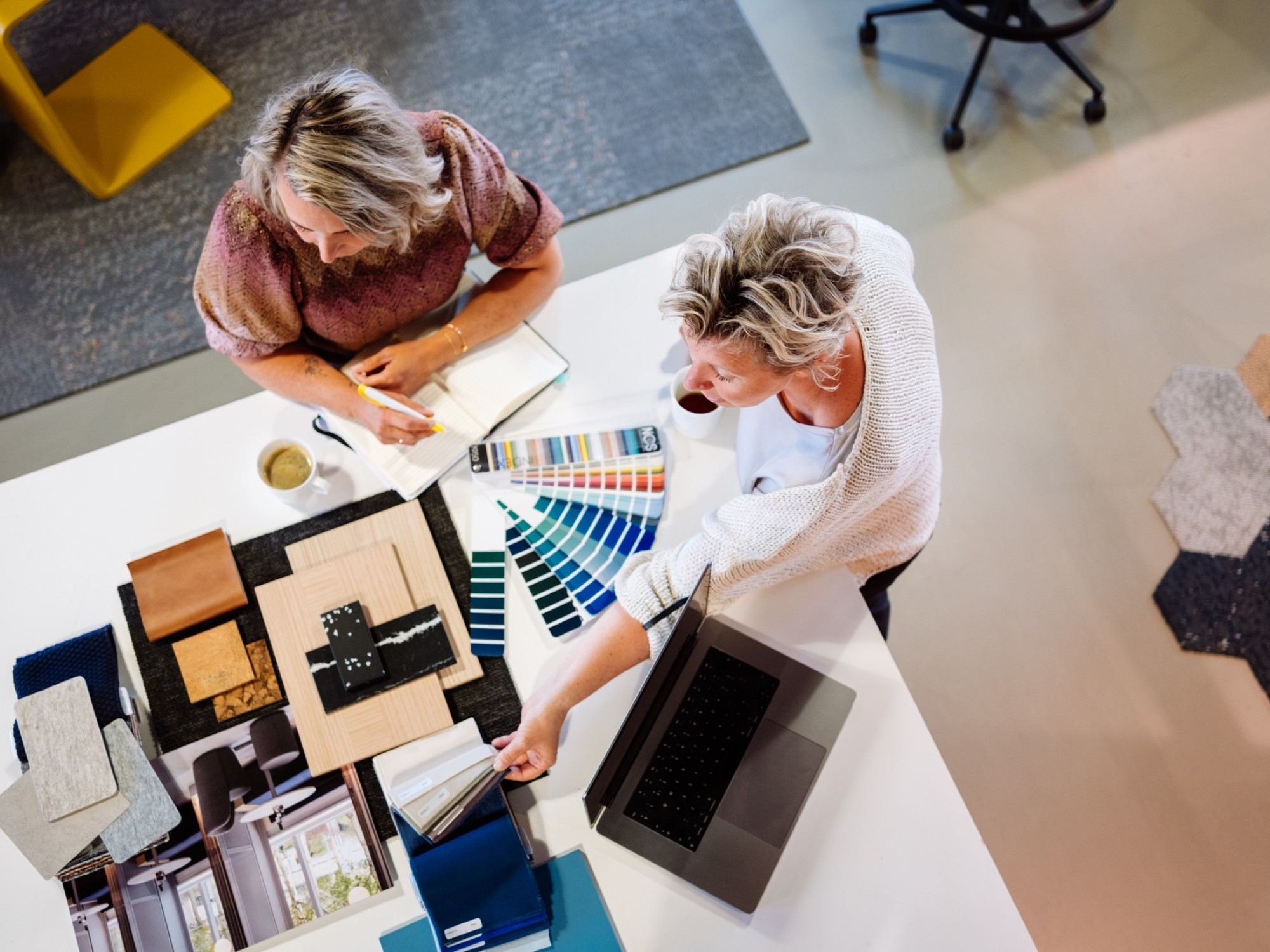 Two designers at a table with colour samples, material swatches and a laptop during a meeting.