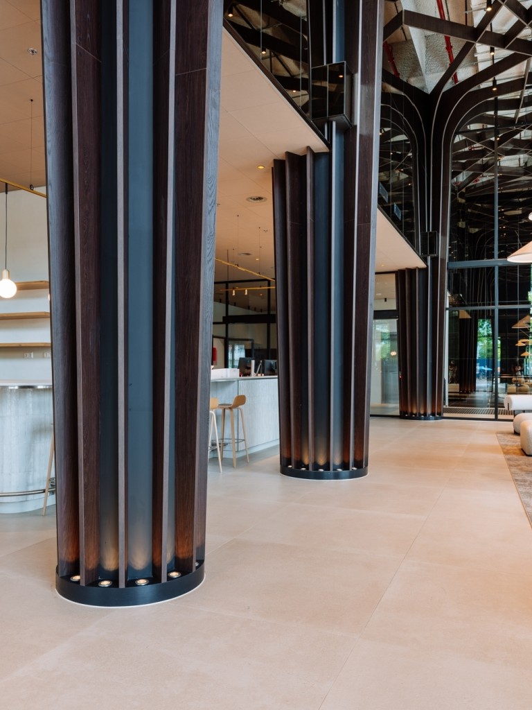 Moderne kantoorlobby met hoge donkere kolommen, designmeubilair en grote glazen gevel bij Wonderwoods.