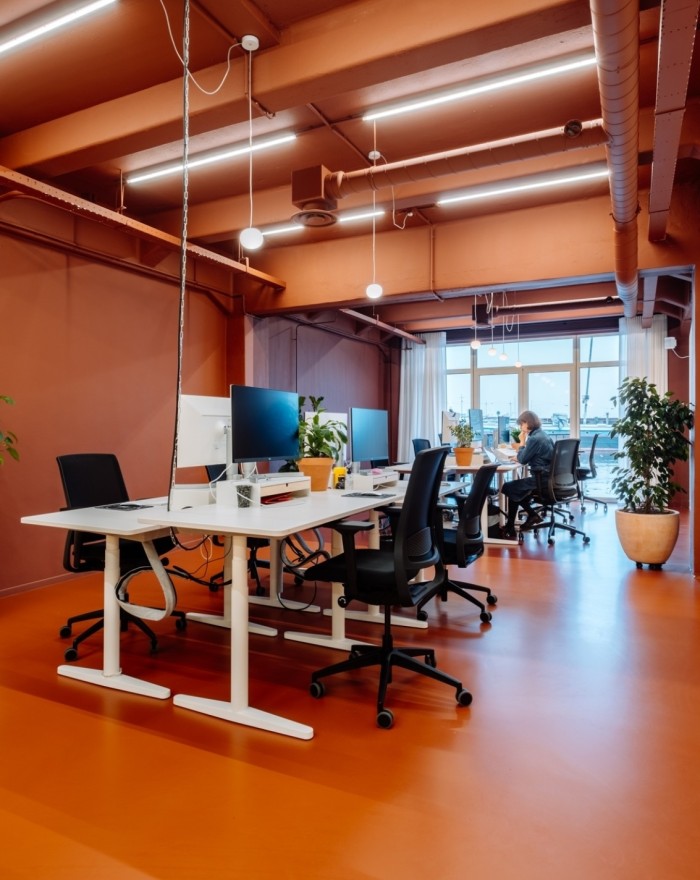 Open kantoorruimte met bureaus, computerschermen en bureaustoelen in een modern interieur met oranje vloer