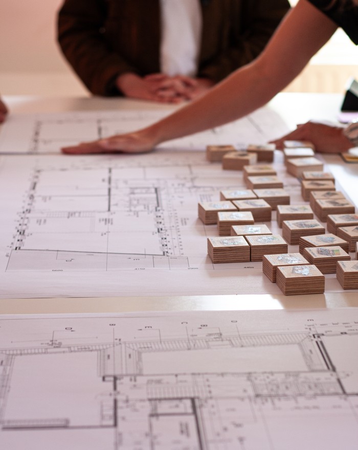 Architecten bekijken bouwtekeningen en houten maquettes op een tafel tijdens een ontwerpsessie
