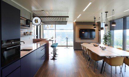 Modern office kitchen and dining area with long table, bar stools and city view