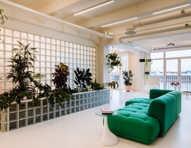 Moderne kantoorinrichting met groene bank, planten in een glazen muur en uitzicht op het water voor Bakken & Baeck door BESPARK