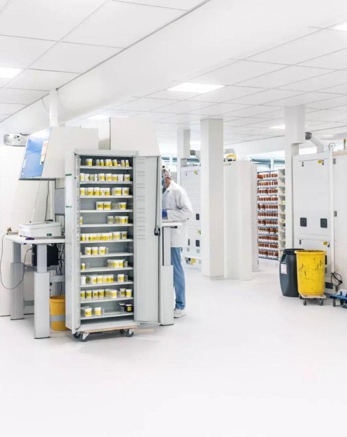 Laboratoriumruimte met medewerker in beschermende kleding bij apparatuur en rekken met monsters