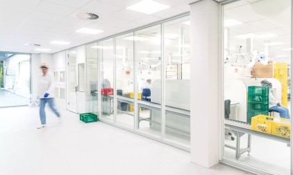 Gang in productiefaciliteit met glazen wanden en zicht op machines en werkstations