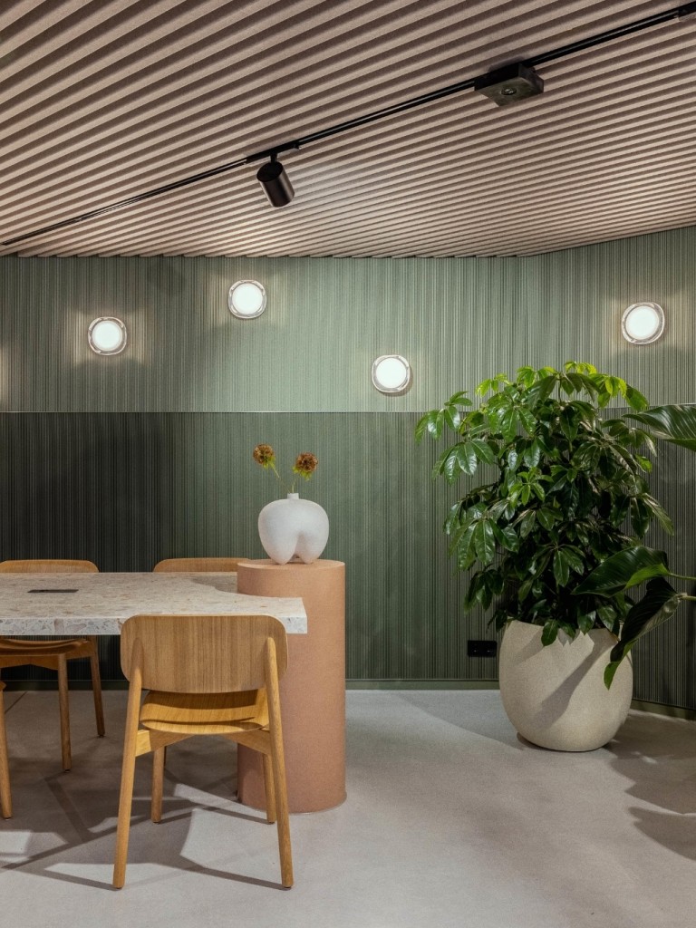 Stijlvolle vergaderruimte met houten tafel en stoelen, groene wandpanelen, moderne verlichting en grote planten voor een rustige, natuurlijke uitstraling.