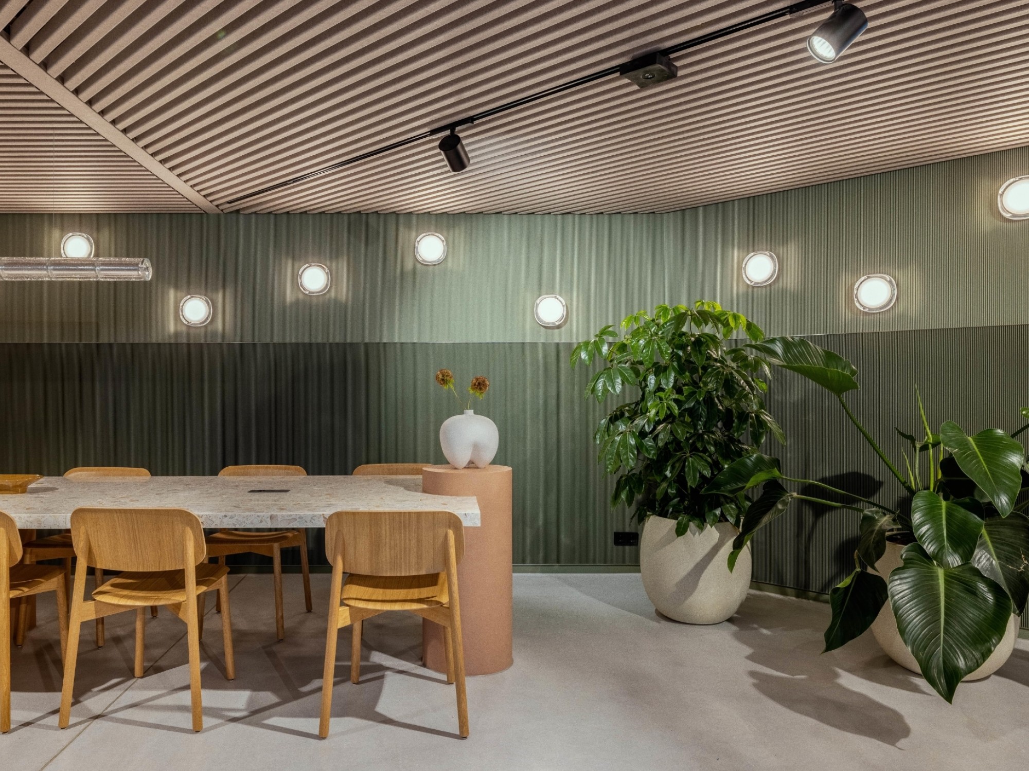 Stijlvolle vergaderruimte met houten tafel en stoelen, groene wandpanelen, moderne verlichting en grote planten voor een rustige, natuurlijke uitstraling.