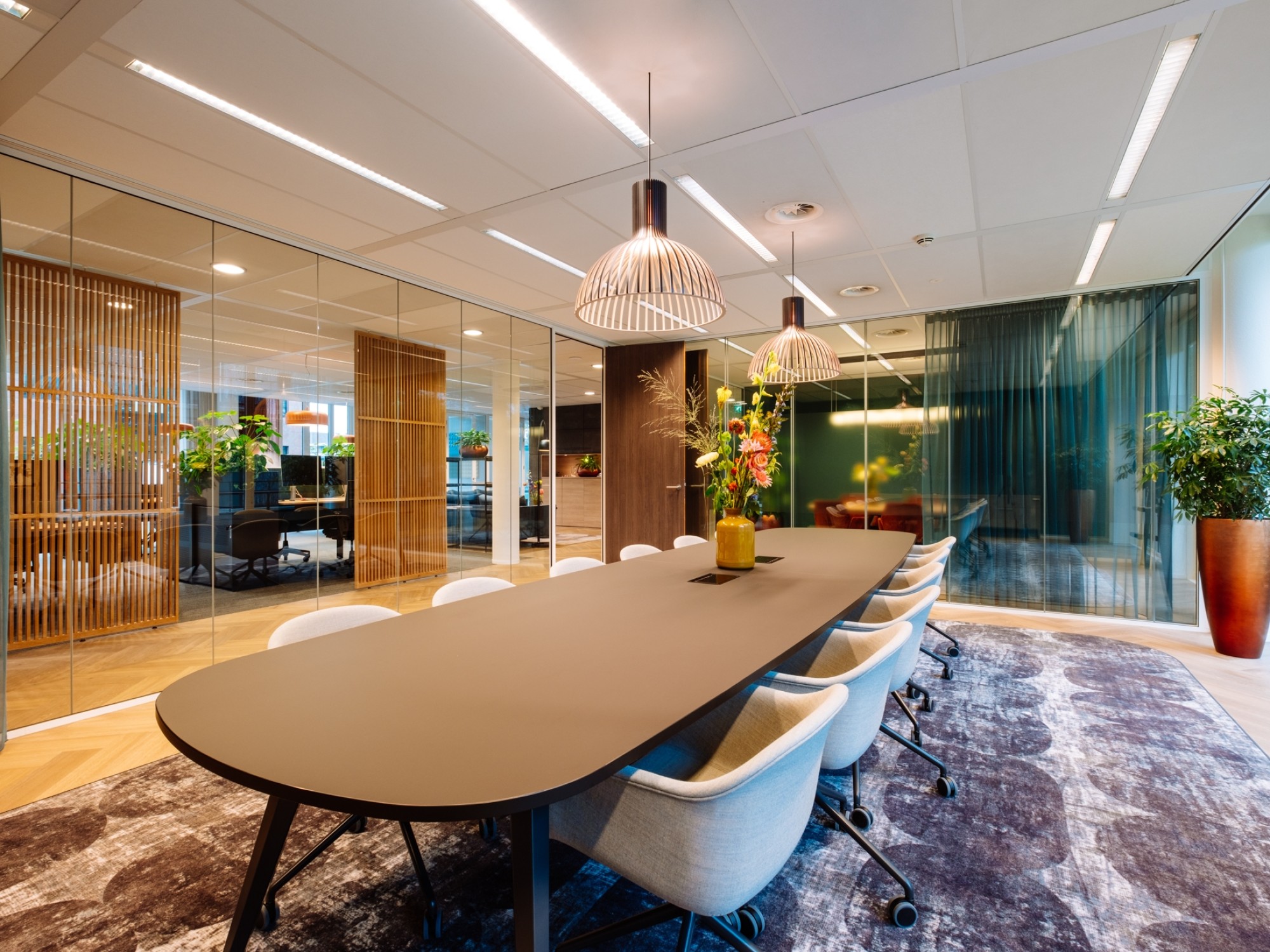 Large meeting room at Bloei Vermogen with a long table, comfortable chairs, warm lighting, and glass walls.