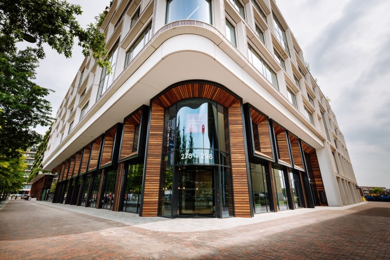 Modern kantoorgebouw met afgeronde glazen hoek, houten geveldetails en grote ramen op straatniveau.