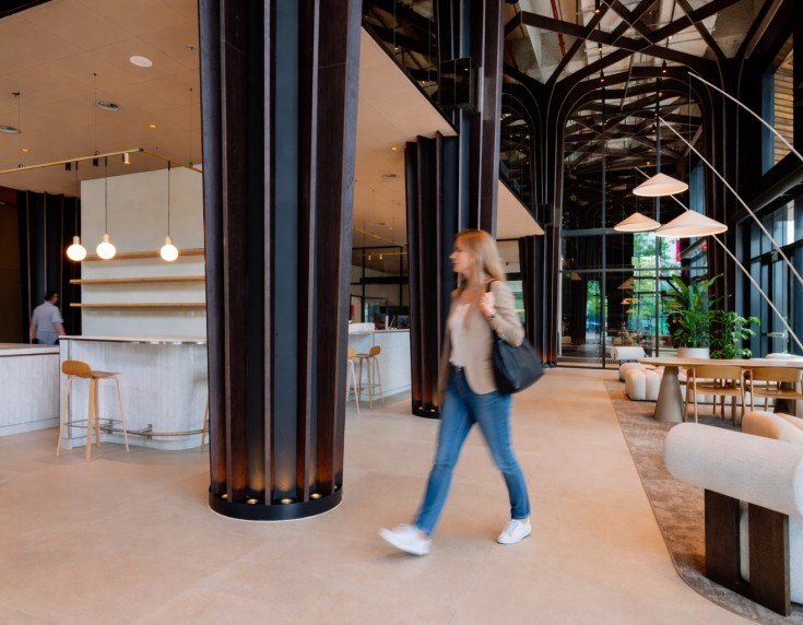 Moderne lobby met hoge plafonds, grote pilaren en open bar- en zithoek, terwijl een persoon door de ruimte loopt.