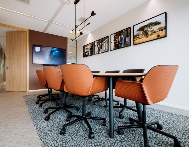 Moderne vergaderruimte met oranje bureaustoelen, houten tafel en groot presentatiescherm aan de muur.