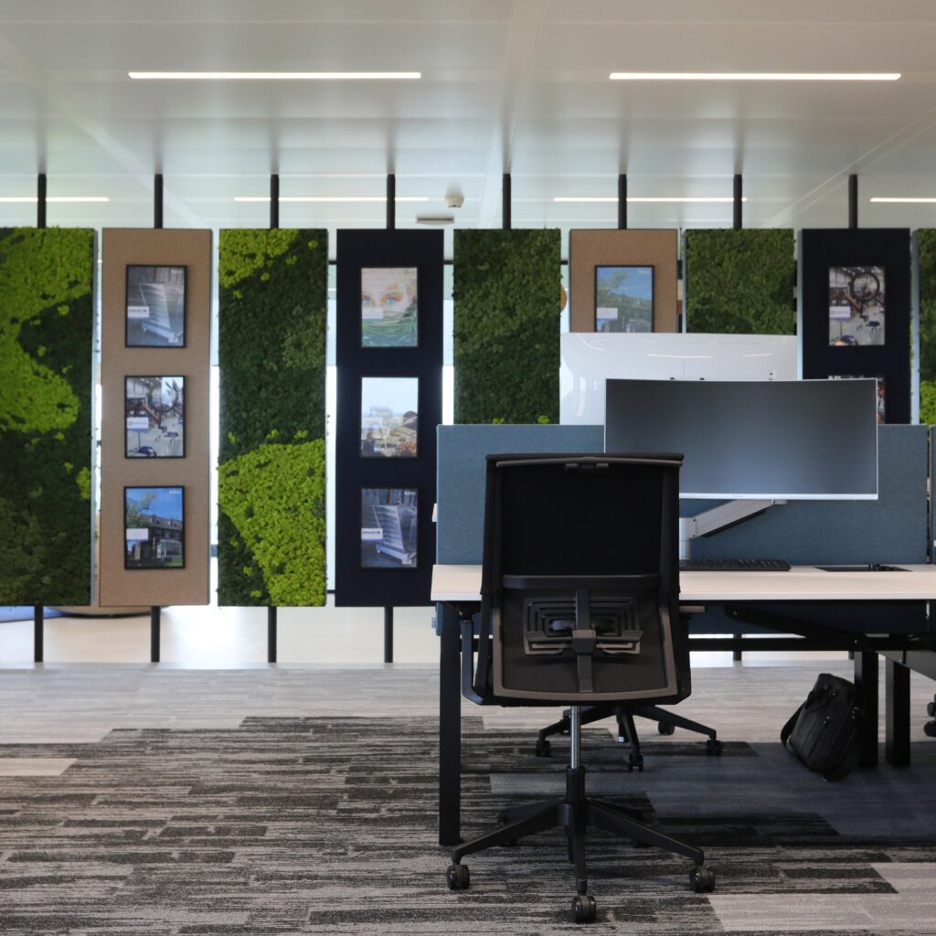 Moderne kantoorruimte met werkplek en groene wandpanelen met foto’s op de achtergrond.