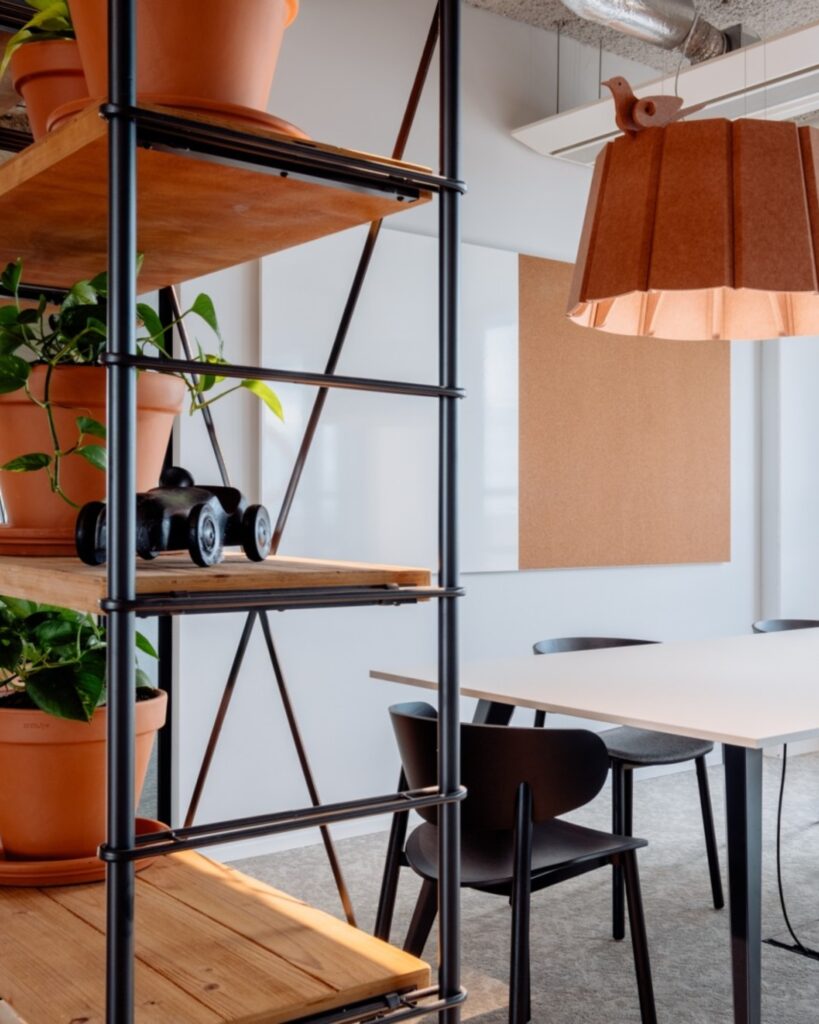 Moderne kantoorhoek met metalen stellingkast, planten en vergadertafel met hanglamp.