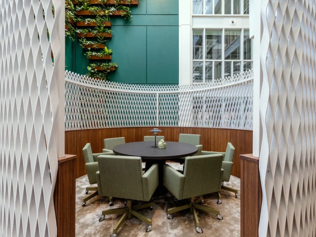 Ronde tafel met groene stoelen in een modern kantoorinterieur, omringd door witte decoratieve panelen en planten aan de muur.