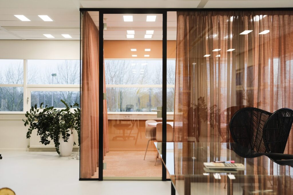 Glazen vergaderruimte met transparante gordijnen en werkplek in moderne kantooromgeving.