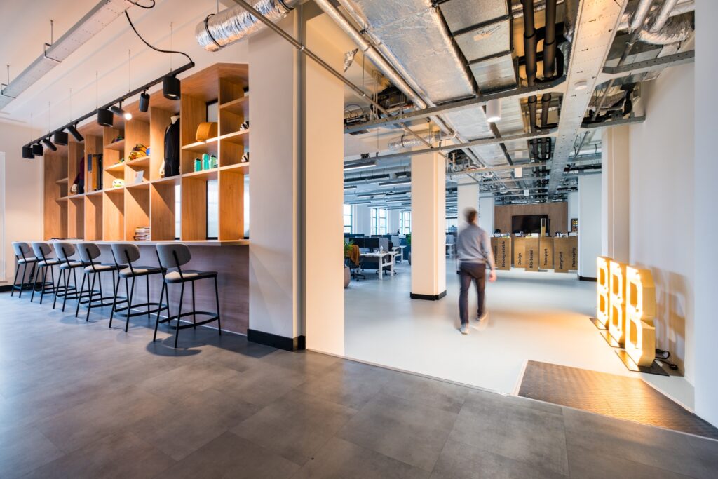 Moderne kantoorruimte met open indeling, hoge kastenwand en barzitplaatsen.