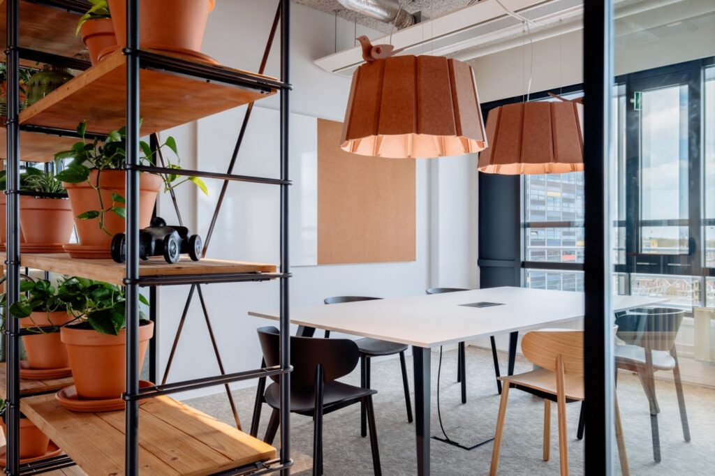 Twee collega’s overleggen aan een hoge tafel in een moderne vergaderruimte met glazen wanden en een betonnen muur. Ze bekijken samen documenten, wat een gefocuste en samenwerkende werksituatie laat zien.