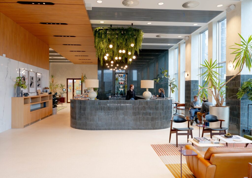 Modern kantoorinterieur met open werkruimte, glazen vergaderruimtes, bureaus en grote groene planten voor een frisse werkomgeving.