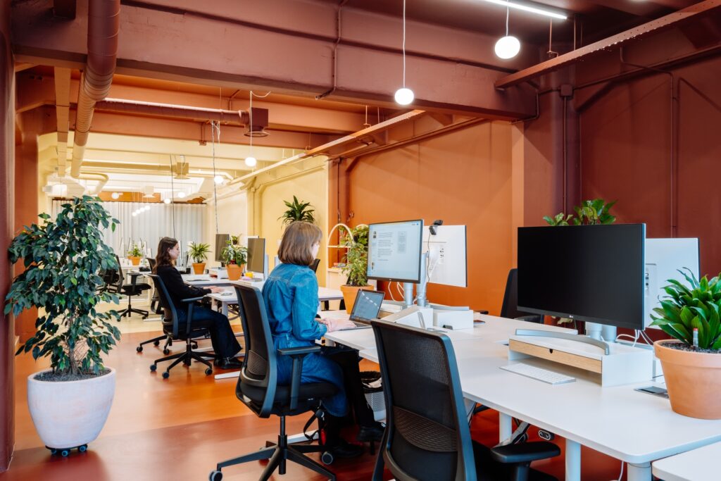 Open kantoorruimte met medewerkers aan bureaus in modern interieur met oranje accenten.