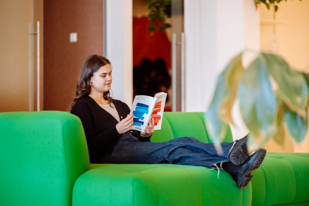 Vrouw leest een tijdschrift op groene bank in moderne kantooromgeving.