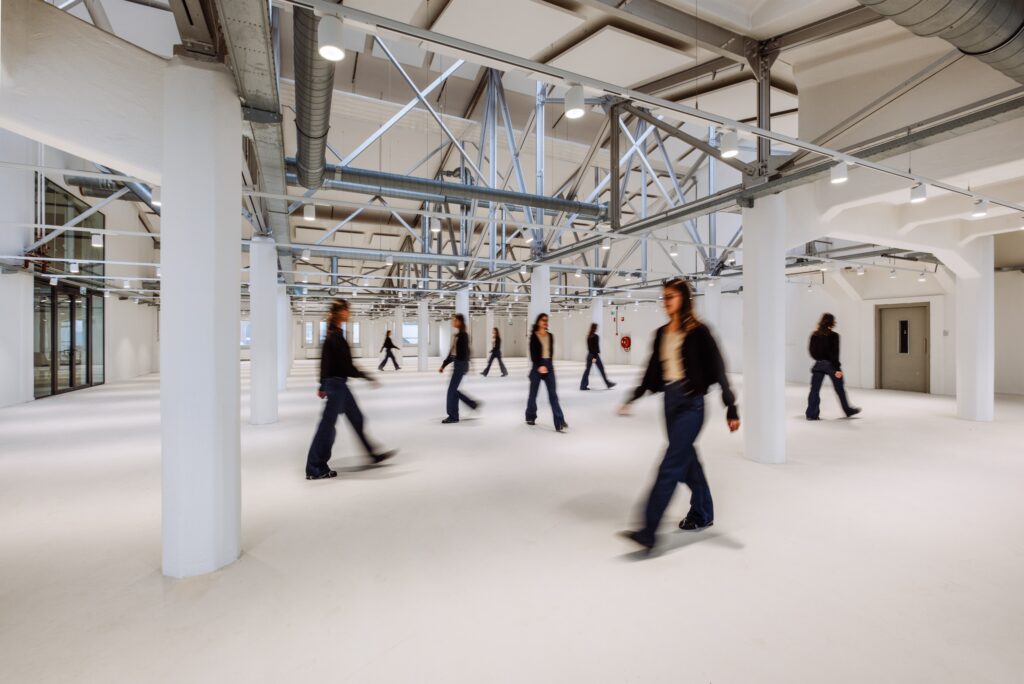 Grote open kantoorruimte met industriële constructie en meerdere personen die door de ruimte lopen.