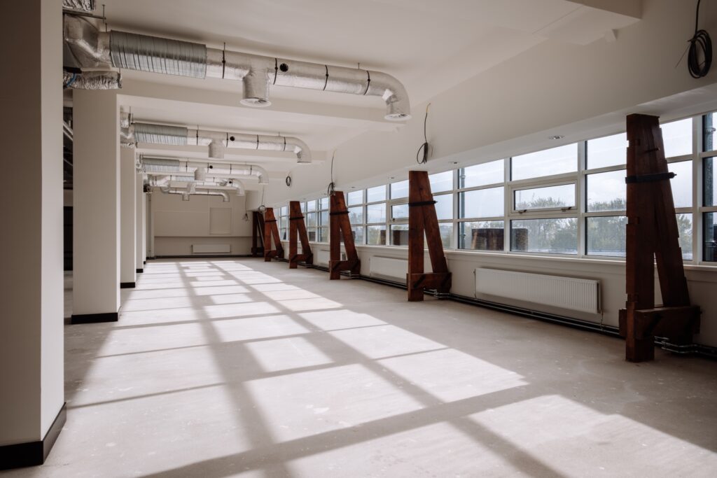 Lege kantoorruimte met grote ramen, veel daglicht en zichtbare ventilatiekanalen.