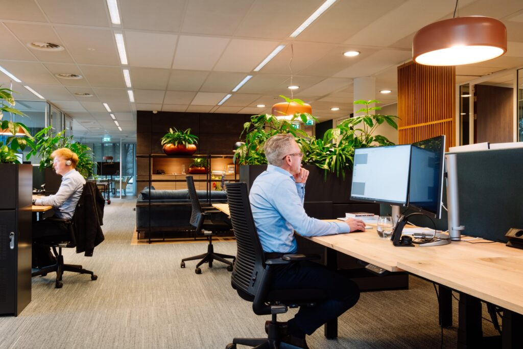 Medewerkers werken aan bureaus in moderne kantoorruimte met planten en warme verlichting.