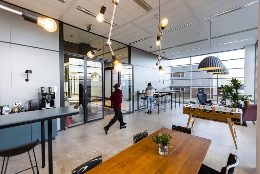 Open kantoorruimte met hoge tafels, hanglampen en medewerkers in informele werkomgeving.