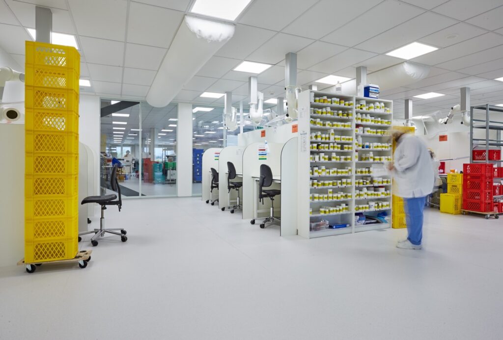 Witte cleanroom met glazen wanden, laboratoriumtafels en heldere verlichting.