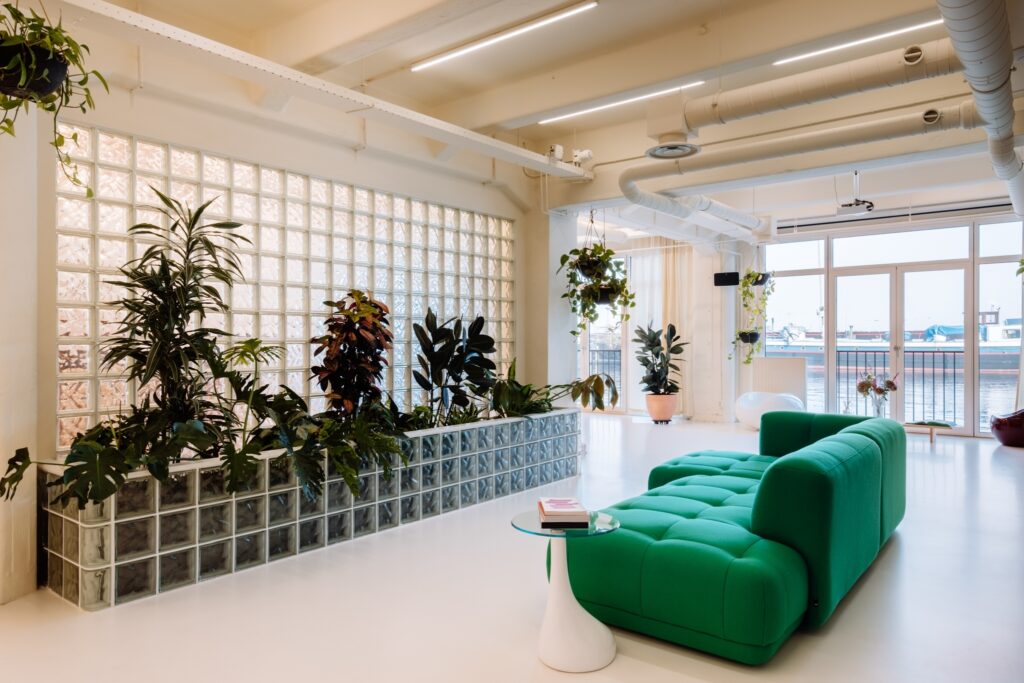 Moderne kantoorinrichting met groene bank, planten in een glazen muur en uitzicht op het water voor Bakken & Baeck door BESPARK