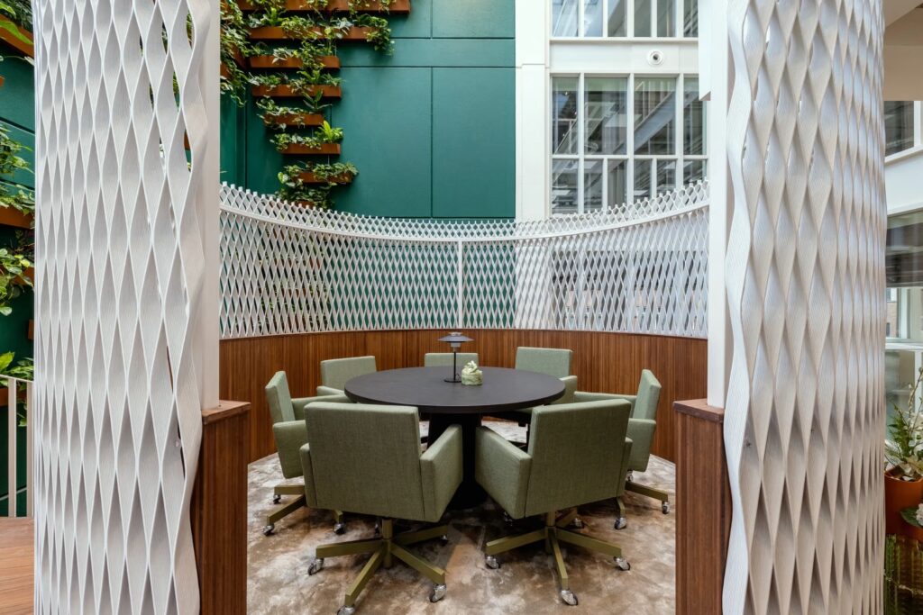 Duurzame vergaderruimte met groene beklede stoelen, houtaccenten en een witte 3D-roomdivider in een groene binnentuinomgeving.
