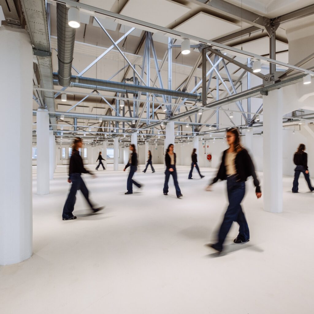 Grote open kantoorruimte met industriële constructie en meerdere personen die door de ruimte lopen.