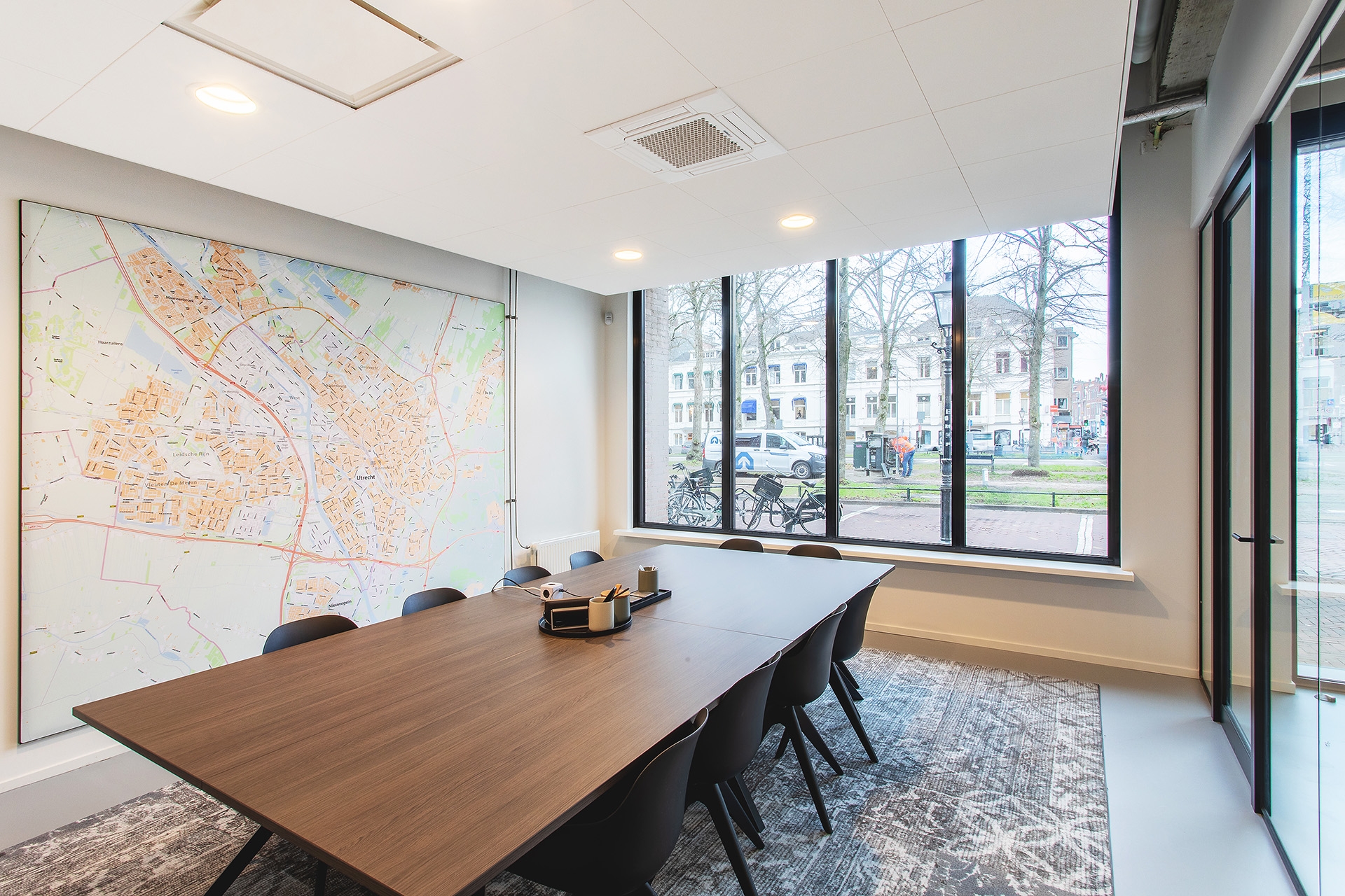 Moderne vergaderruimte met grote tafel, wandkaart en grote ramen met uitzicht op buiten, voorzien van veel daglicht.