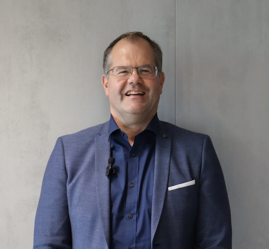 Portret van een man in blauw colbert tegen een neutrale achtergrond.