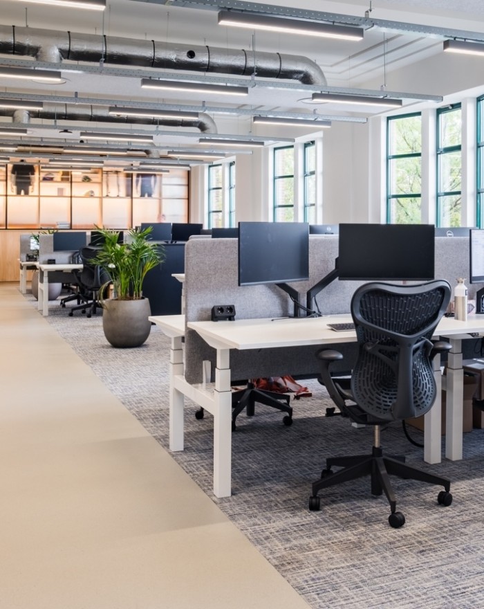 Modern kantoorinterieur met bureaus, ergonomische stoelen en groene planten.