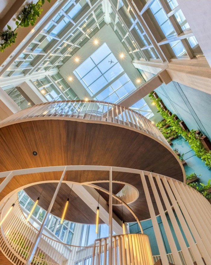Spiraalvormige houten trap in een modern, groen atrium met glazen plafond.