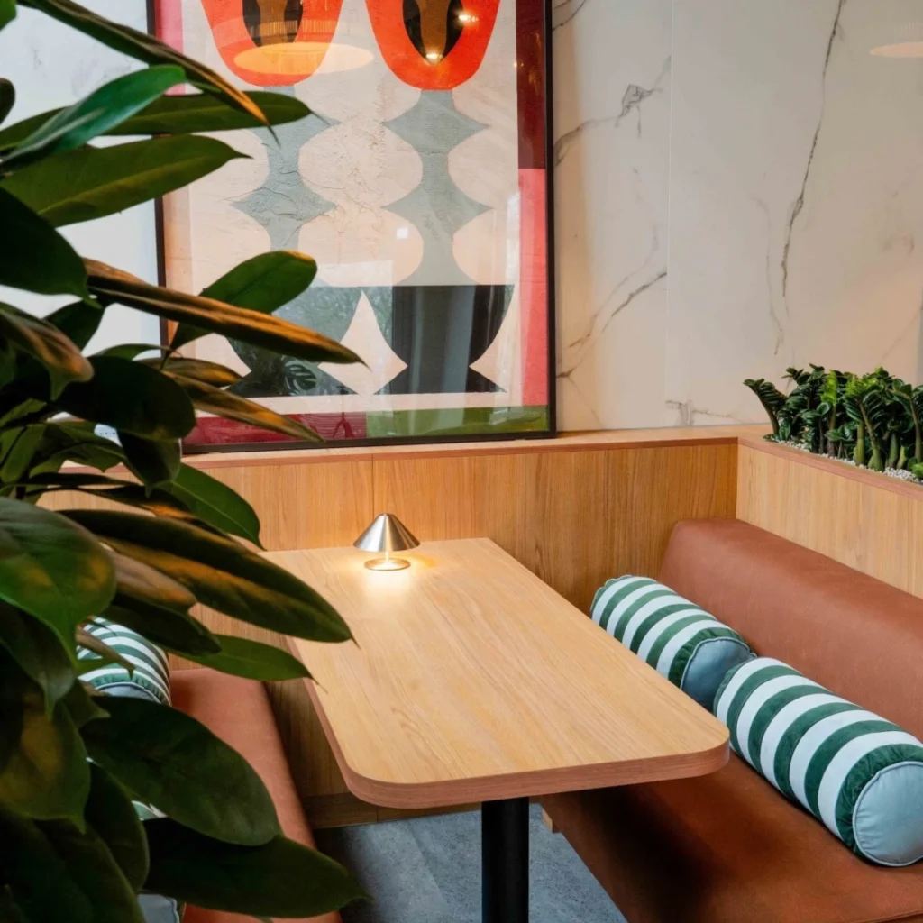 Gezellige zithoek met houten tafel, kunstwerk aan de muur en groen gestreepte kussens.