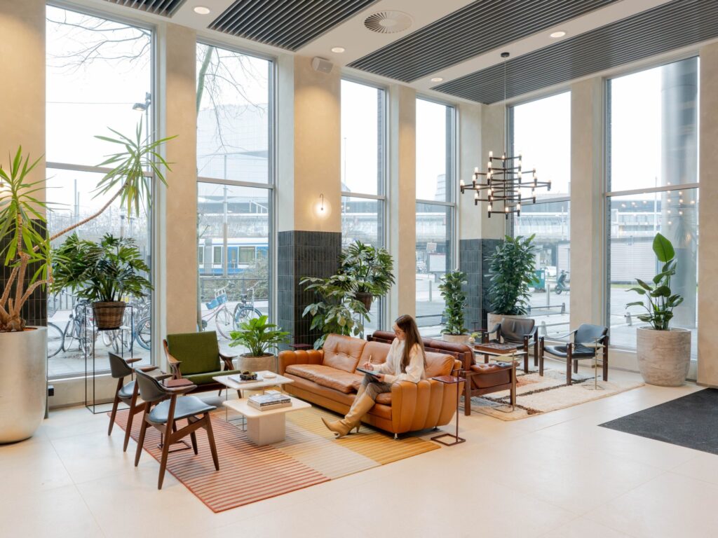 Een vrouw leest op een leren bank in een moderne, lichte lobby vol met planten.