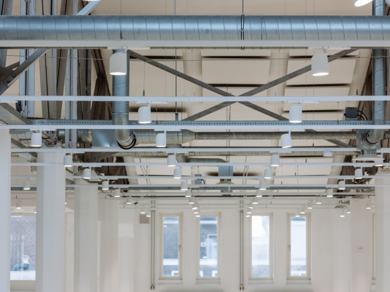 Industriële binnenkant van een moderne ruimte met zichtbare buizen, balken en verlichtingsarmaturen in de Houthavens.